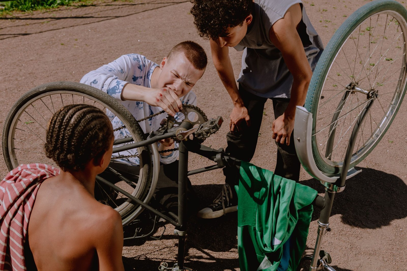 Three young men fixing a bike outdoors on a sunny day, teamwork and repair concept.